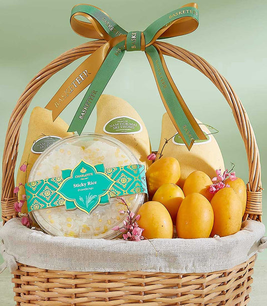 Woven wicker gift basket with premium Thai mangoes, sticky rice, and pink flowers tied with gold and green Basketeer ribbons