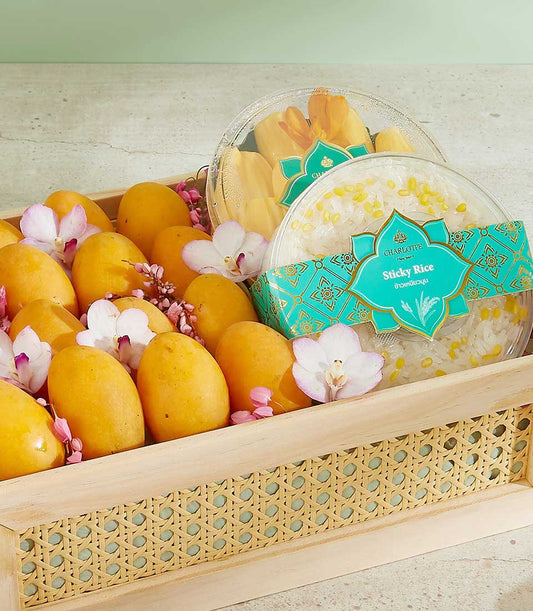 Authentic Mayongchid Thai fruit gift basket with yellow mangoes, jackfruit, sticky rice, and purple orchids on woven wooden