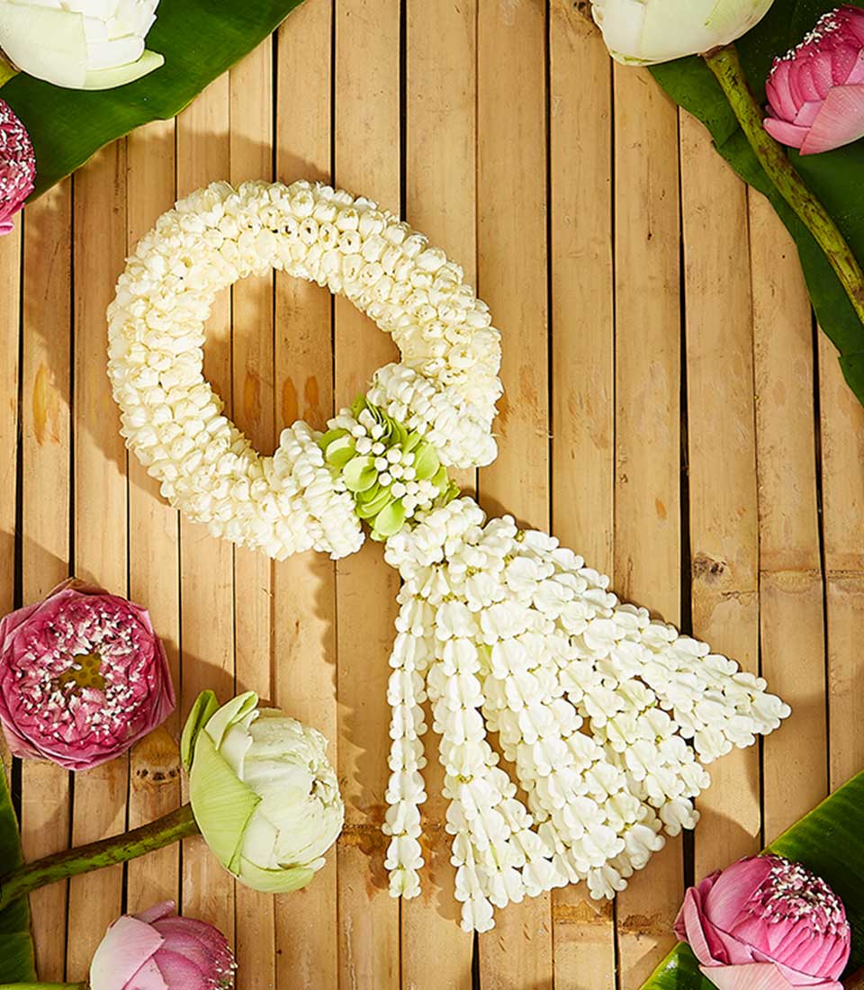 White jasmine phuang malai garland with cascading buds and pink lotus flowers on bamboo mat, Thai New Year Songkran gift