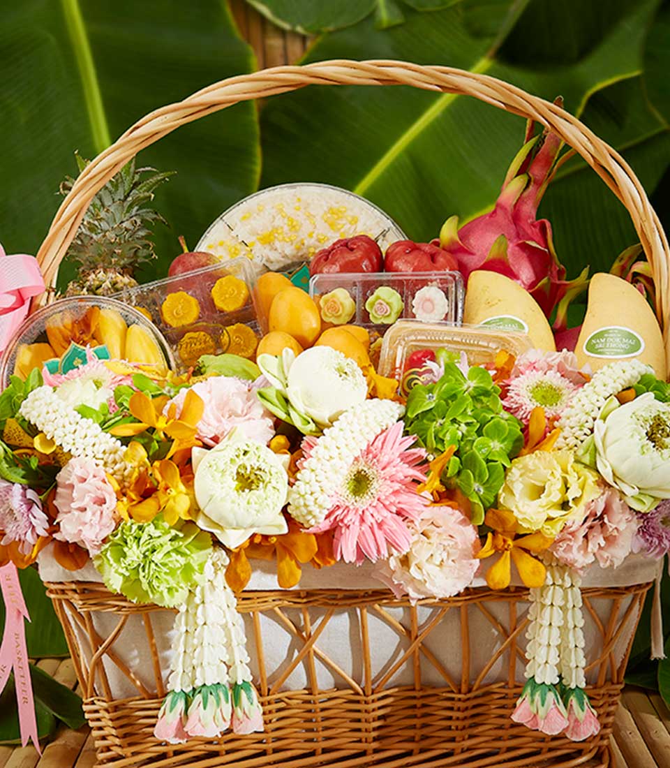 Wicker basket filled with fresh tropical fruits, Thai desserts, and fresh flowers in white, pink, and yellow for Thai New