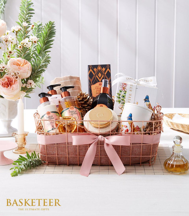 Luxe rose gold spa basket with bath products, cream lotion bottles, gold jar, perfume, and pink satin bow