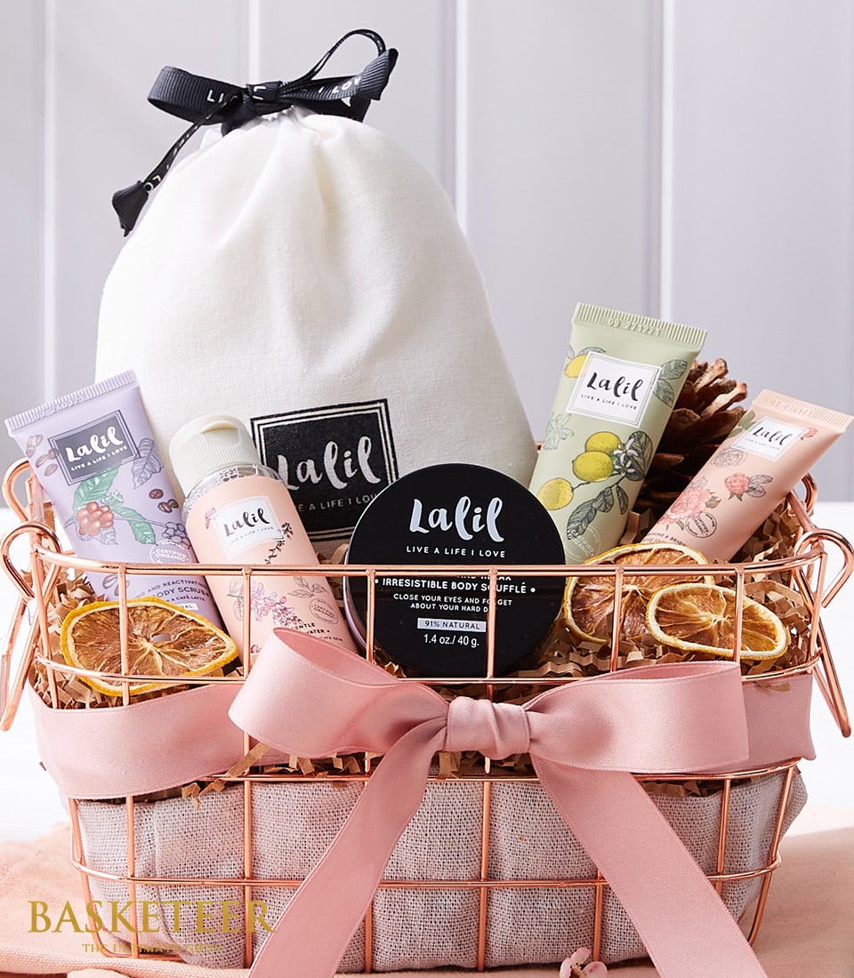 Luxury spa gift basket with rose gold wire container, cream drawstring bag, bath and body products, pink satin ribbon, and