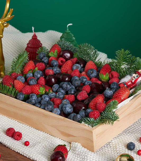 Festive wooden box overflowing with fresh strawberries, blueberries, raspberries, and cherries with pine sprigs for Christmas