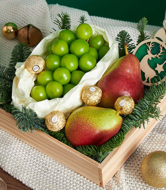 Festive wooden tray with green plums, pears, Ferrero Rocher chocolates, and pine sprigs for Christmas