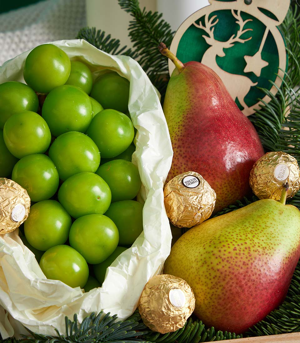 Festive fruit gift box with green plums, pears, and Ferrero Rocher chocolates nestled in pine