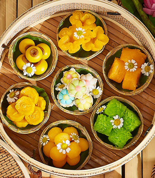 Artisan Thai dessert gift set in seven woven bamboo baskets with banana leaf linings and fresh daisy flowers, perfect for
