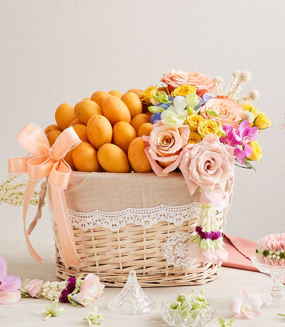 Woven wicker gift basket with fresh yellow mangoes, peach and pink roses, orchids, and Thai floral garland for Songkran New