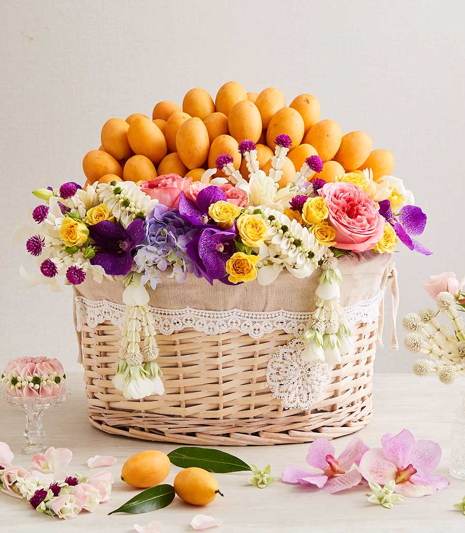 Woven wicker basket overflowing with golden Marian plums, topped with purple orchids, pink and yellow roses, and white