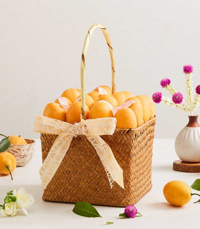 Woven straw basket of golden marian plums wrapped with pink ribbons and cream floral bow