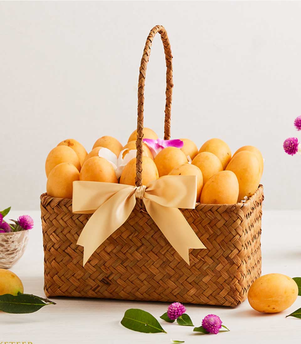 Woven straw basket overflowing with ripe yellow mangoes, purple orchids, and golden satin bow