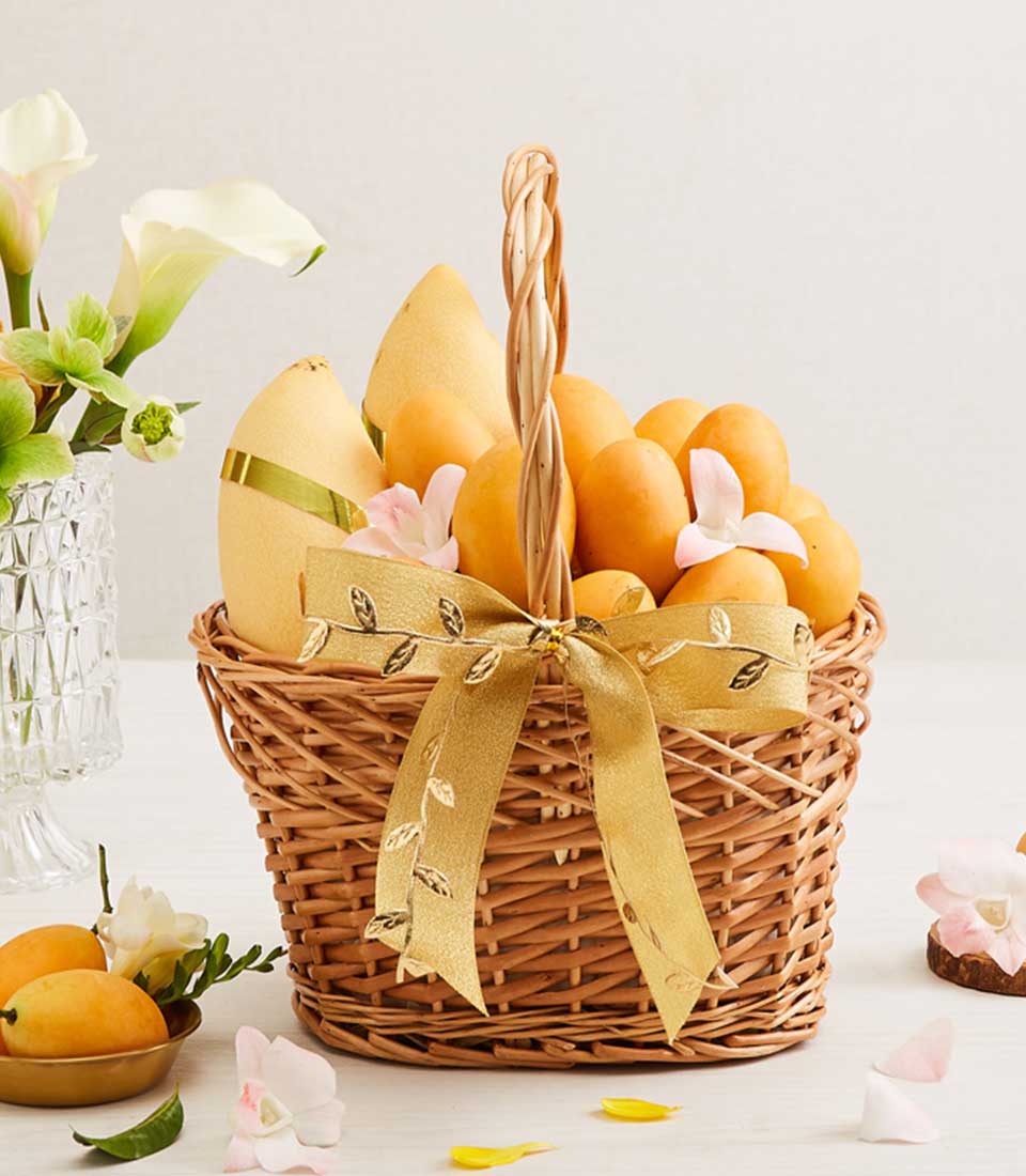 Golden wicker fruit basket filled with ripe yellow and orange mangoes, pink orchids, and golden ribbon bow