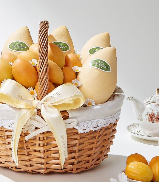 Luxury wicker fruit basket with premium Nam Doc Mai mangoes, fresh daisy flowers, and cream satin bow
