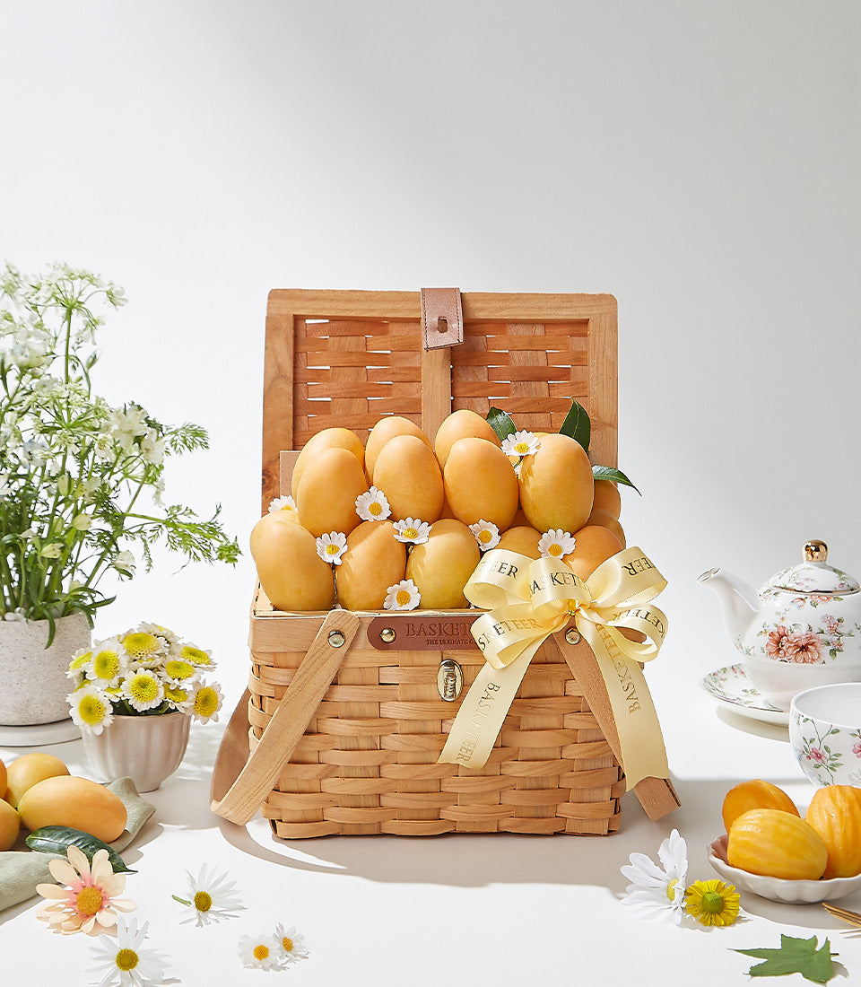 Woven picnic basket filled with ripe golden mangoes, white daisies, and yellow ribbon bow