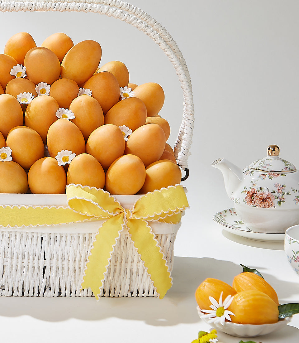 Deluxe white wicker basket overflowing with tropical orange fruits and white daisies, tied with sunny yellow ribbon