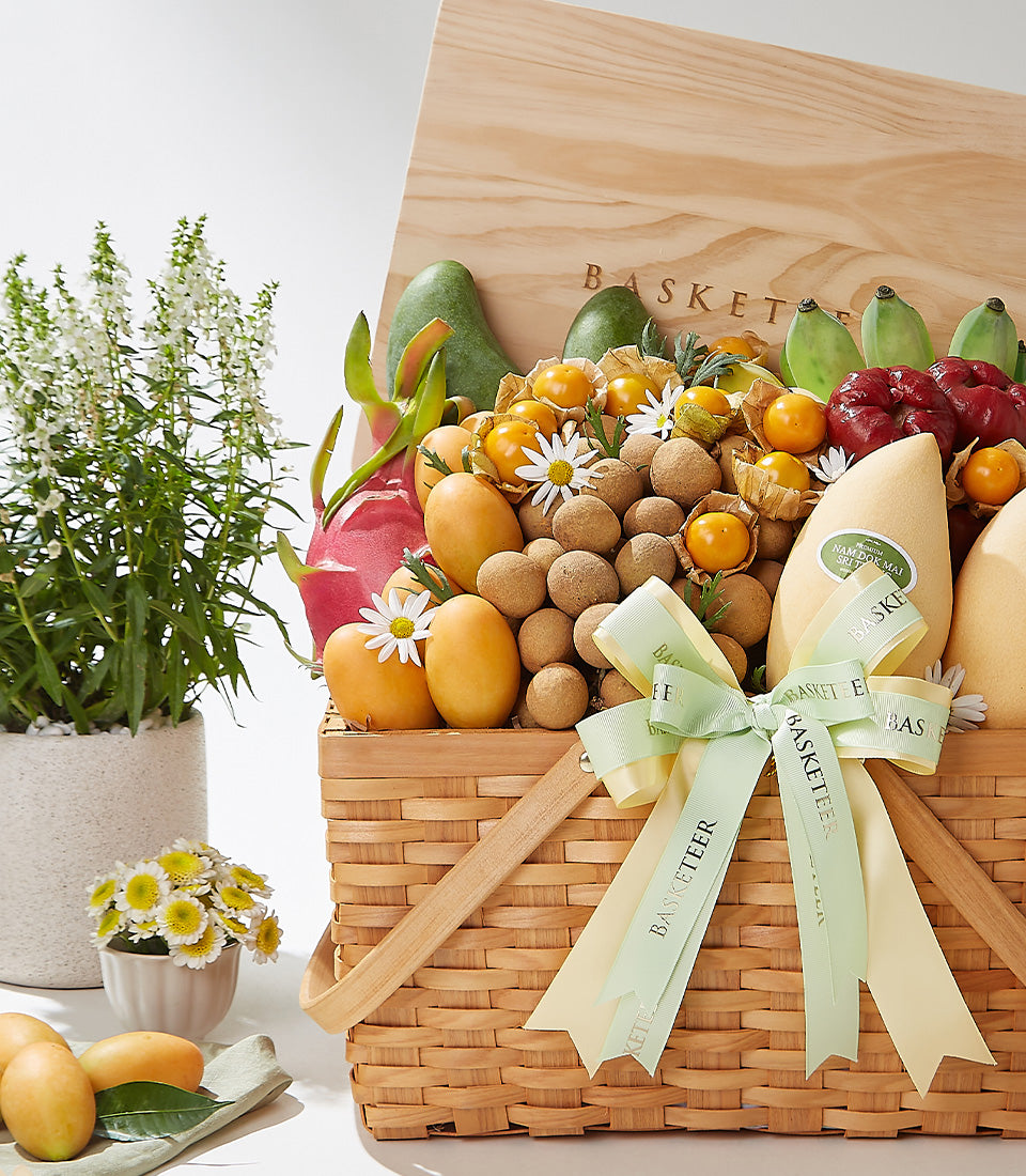 Woven wicker basket overflowing with Thai tropical fruits—mangoes, dragon fruit, longans, and physalis with white daisies