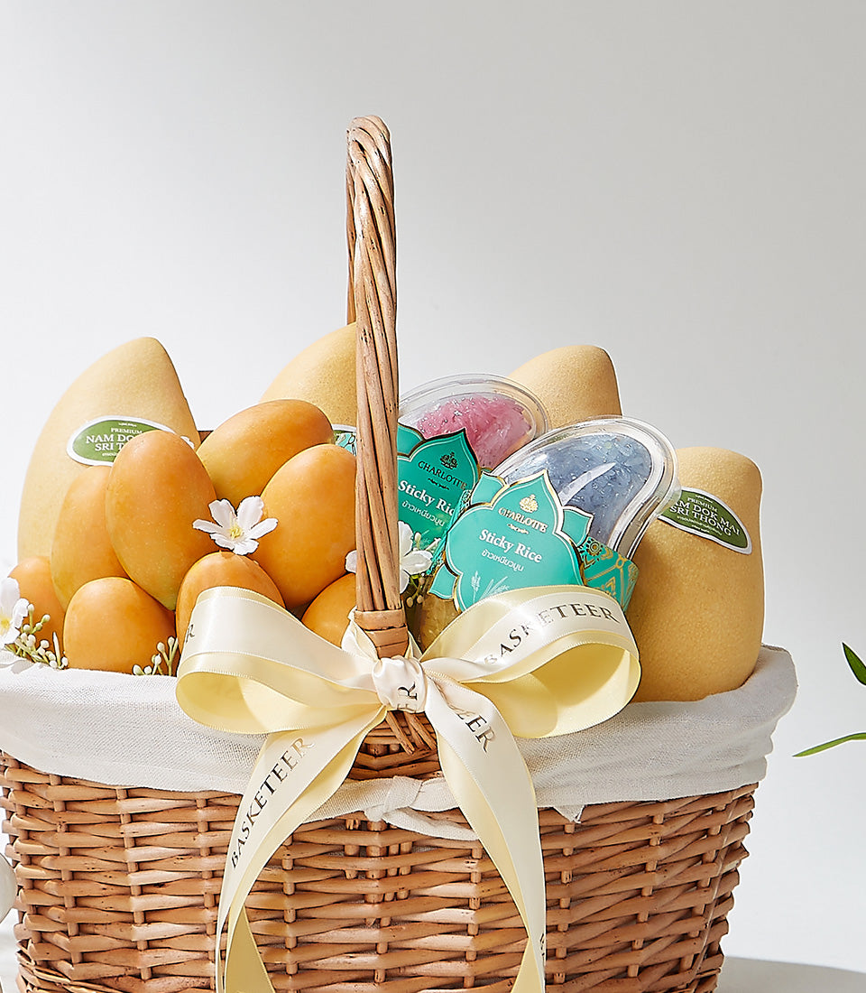 Woven wicker basket filled with Thai mangoes, sticky rice desserts, and fresh flowers