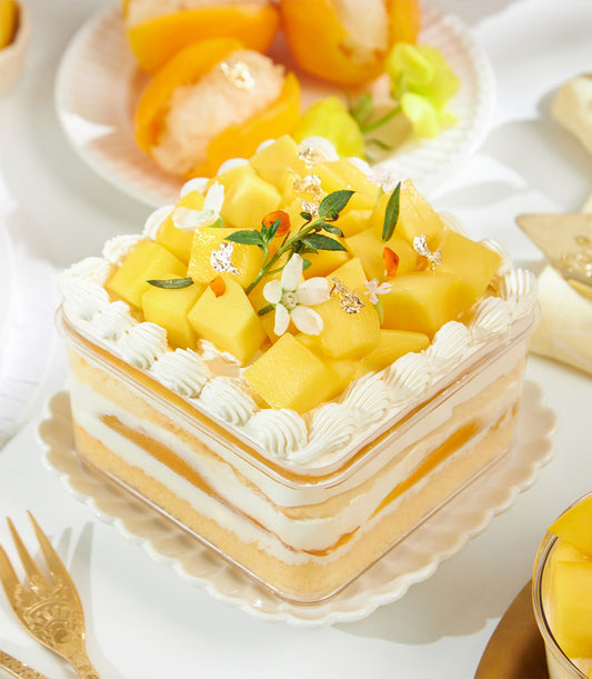 Golden mango layered cake with fresh mango, cream, and edible flowers in clear box