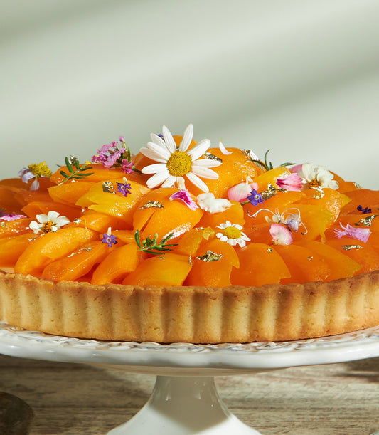 Golden apricot cheese tart with edible flowers and gold leaf on ceramic stand