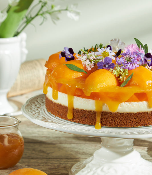 Biscoff cheesecake with caramelized apricots, crumbly crust, and fresh purple, white, and pink flowers on ceramic stand