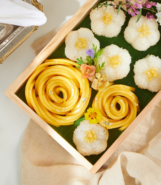 Golden mango sticky rice box with floral sticky rice portions, silver leaf, and fresh flowers on banana leaf tray