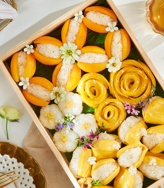 Golden Thai sticky rice celebration box with mango, jackfruit, and edible gold leaf on banana leaf tray