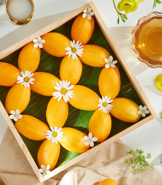 Premium yellow mango gift tray with fresh daisy flowers on banana leaf, tropical luxury presentation