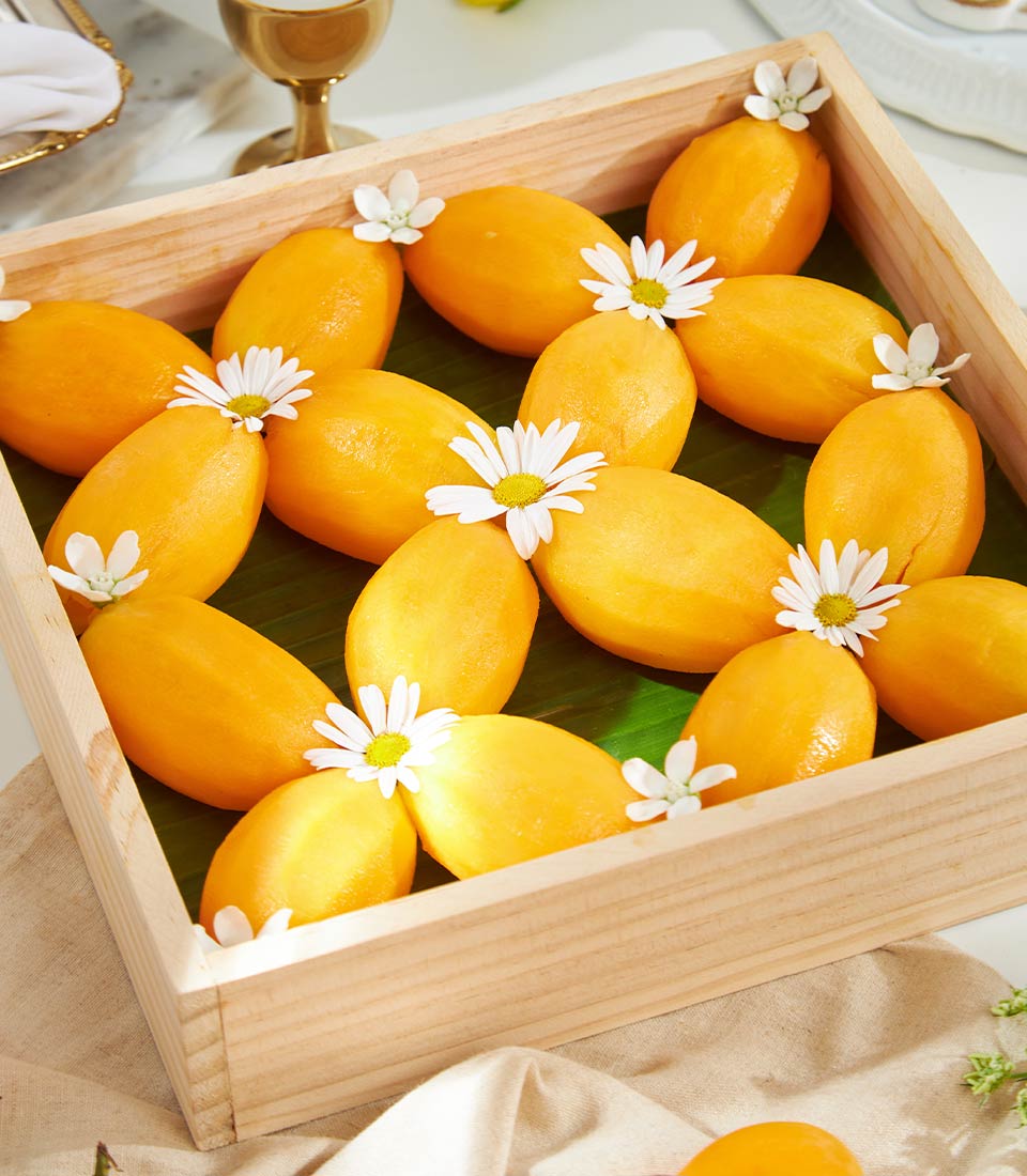Peeled yellow tropical fruits with white flowers on green banana leaf in wooden gift tray