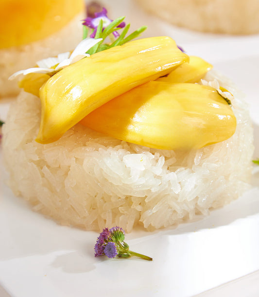Mango sticky rice dessert with ripe mango slices, white sticky rice, and edible flower garnish on white plate