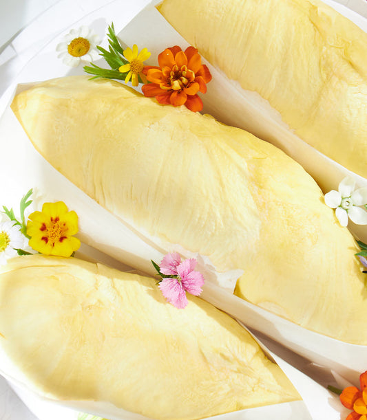 Pale yellow Rayong Mon Thong durian pods wrapped in white paper with scattered fresh flowers on white surface