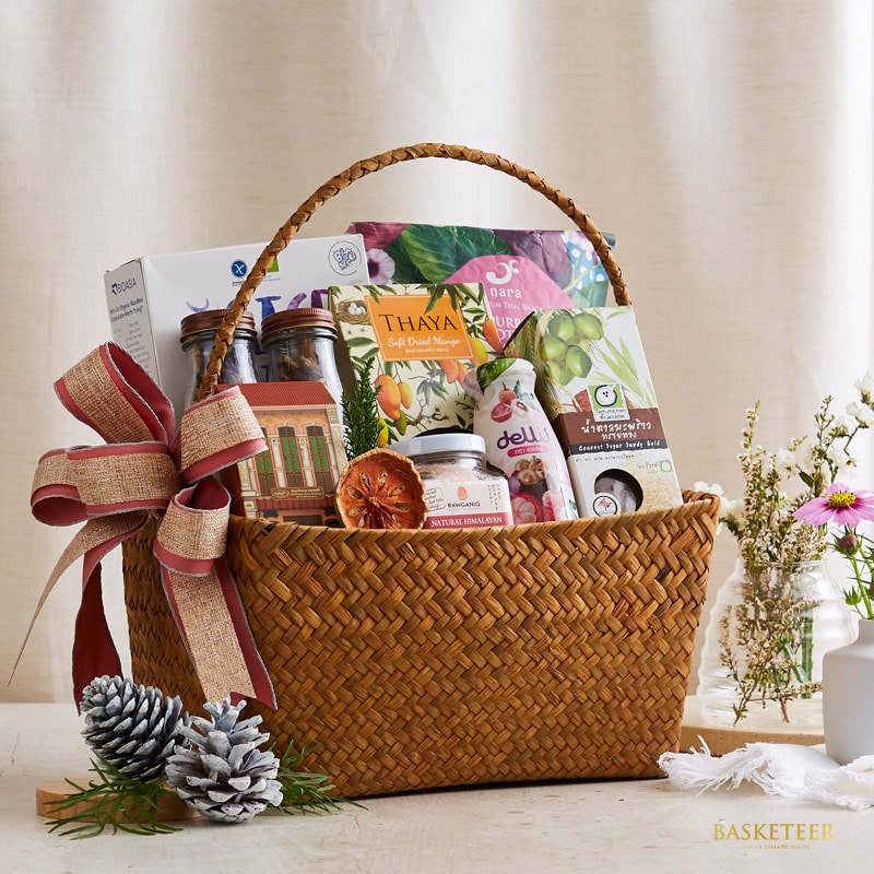 Woven natural fiber gift basket with red burlap bow, filled with gourmet Thai treats and artisan foods