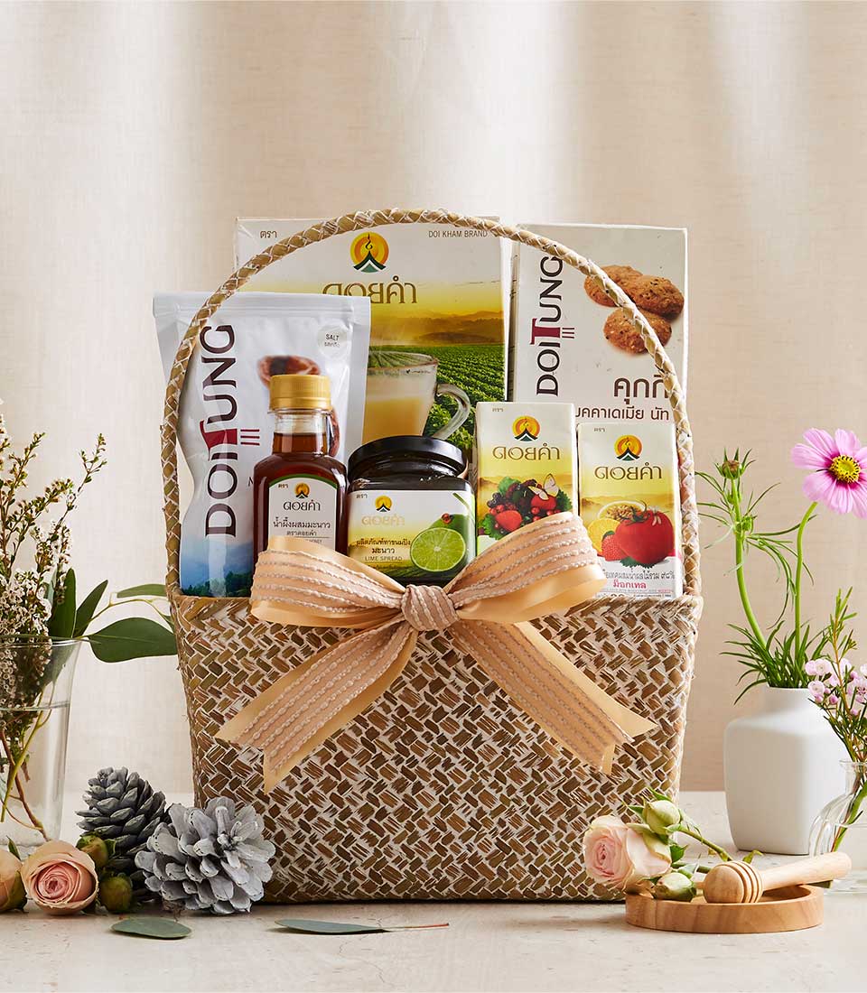 Woven straw gift basket tied with peach ribbon, filled with Doi Tung and Doi Kham gourmet products including artisan