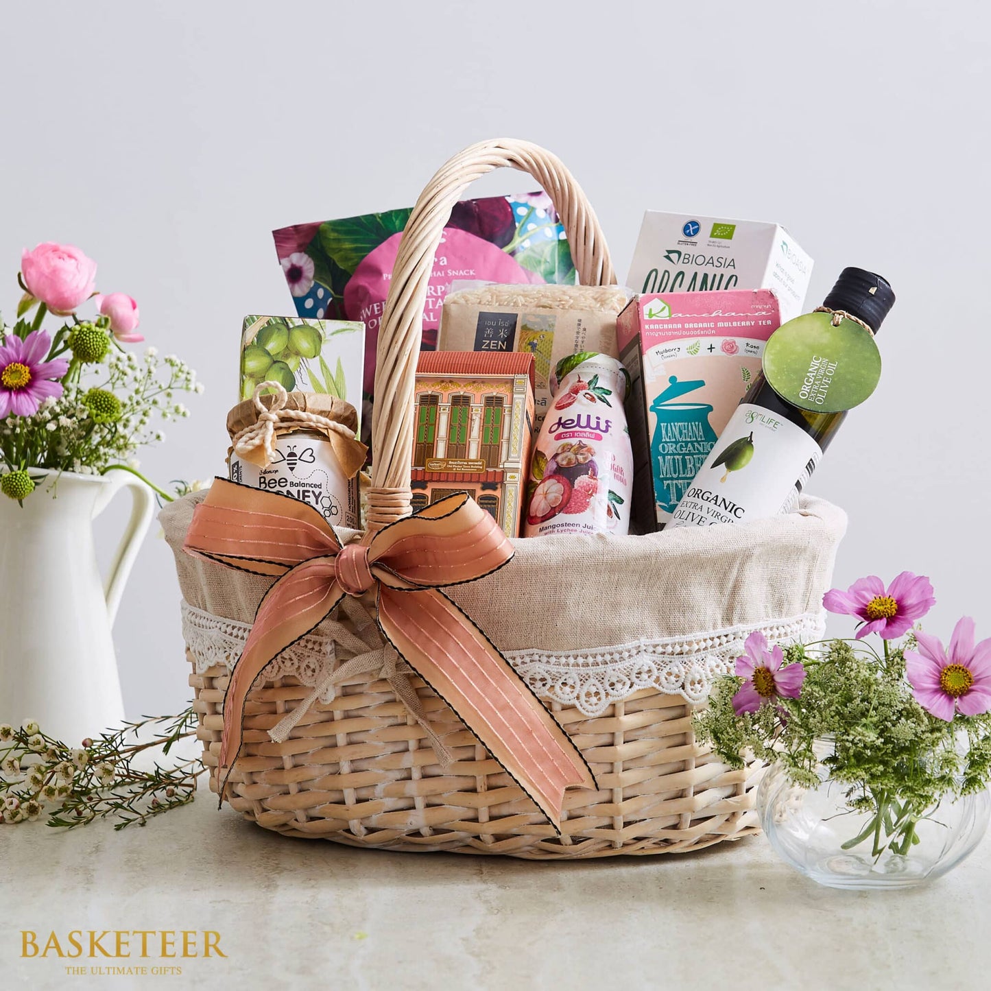 Wicker gift basket with Thai products, peach ribbon, lace trim. Basketeer premium hamper includes honey, olive oil and local treats. Perfect Bangkok gift.