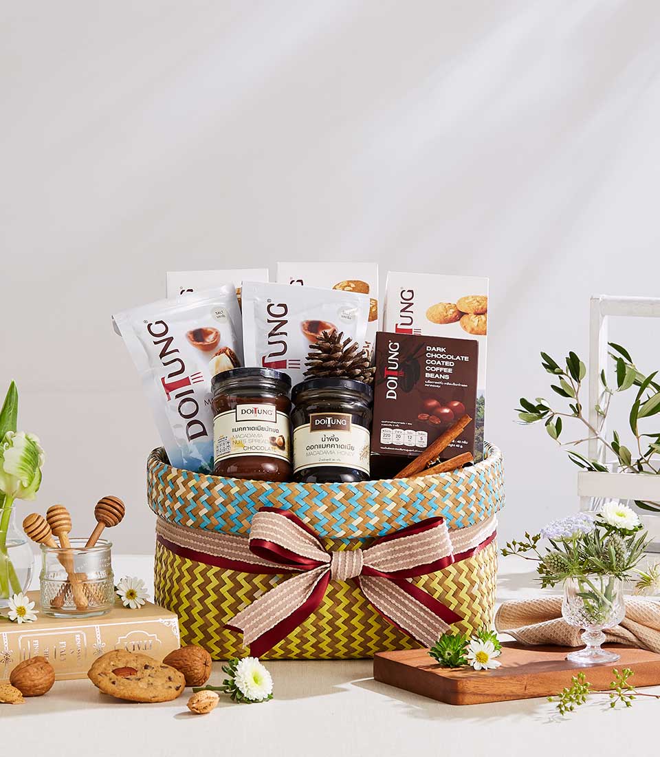 Woven gift basket with Doi Tung gourmet treats, macadamia spreads, coffee beans, and wellness items tied with striped ribbon