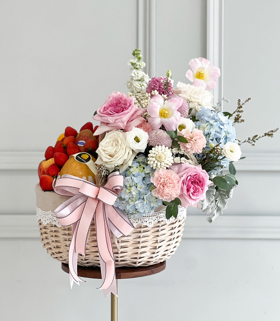 Wicker fruit and flower gift basket with fresh strawberries, pears, and peaches alongside pink roses, white dahlias, and