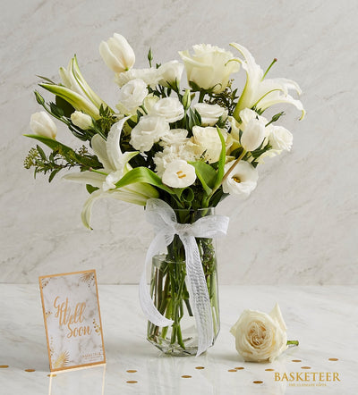 Pure white roses, lilies, and tulips in clear glass vase with sheer ribbon bow