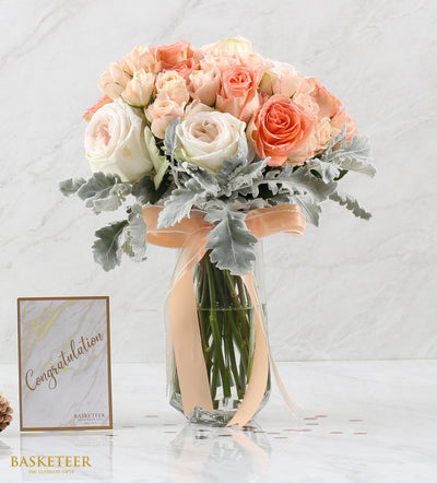 Premium rose bouquet in glass vase with white, pink, and coral blooms, dusty miller, and peach ribbon