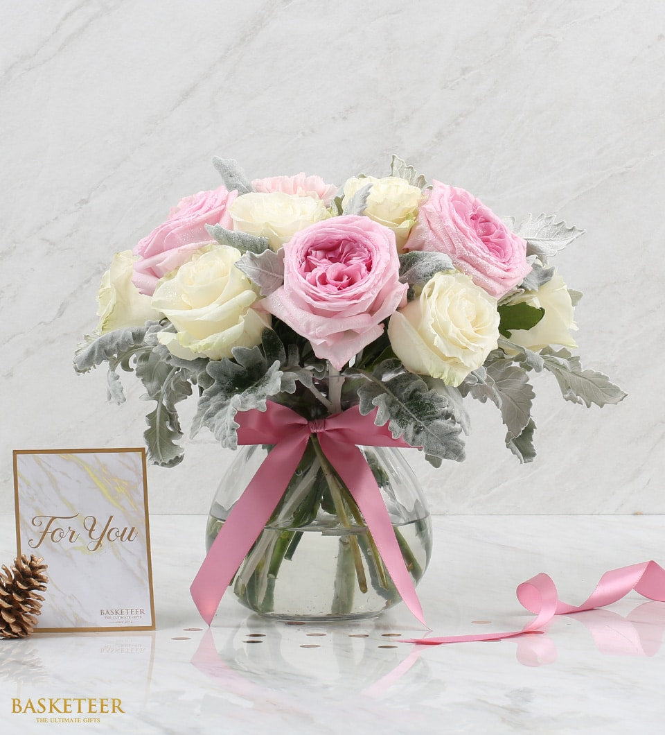 Fresh blush and cream roses in clear glass vase with dusty miller and pink satin ribbon