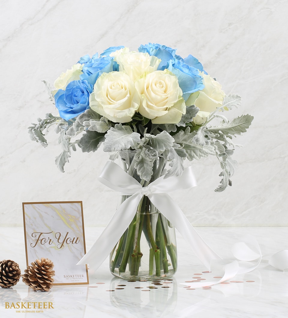Light blue and cream roses in glass vase with dusty miller, white satin ribbon, and rose gold accents