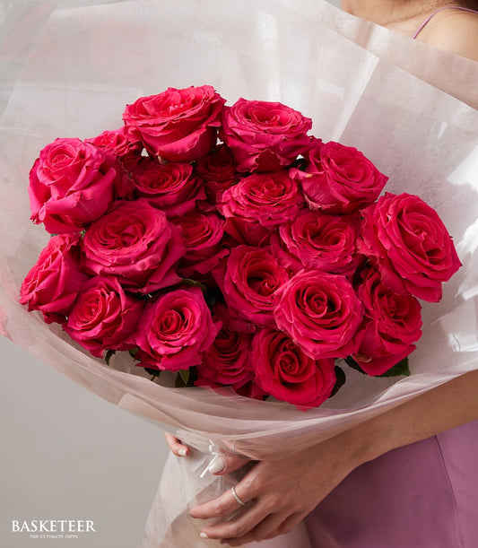 Vivid hot pink rose bouquet with layered petals and green foliage wrapped in white paper for anniversaries