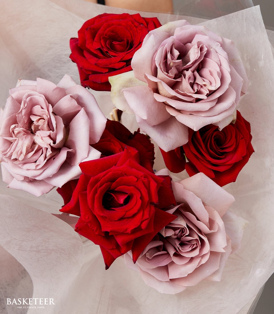 Red and dusty pink roses bouquet wrapped in white crinkled paper, premium fresh flowers for anniversaries