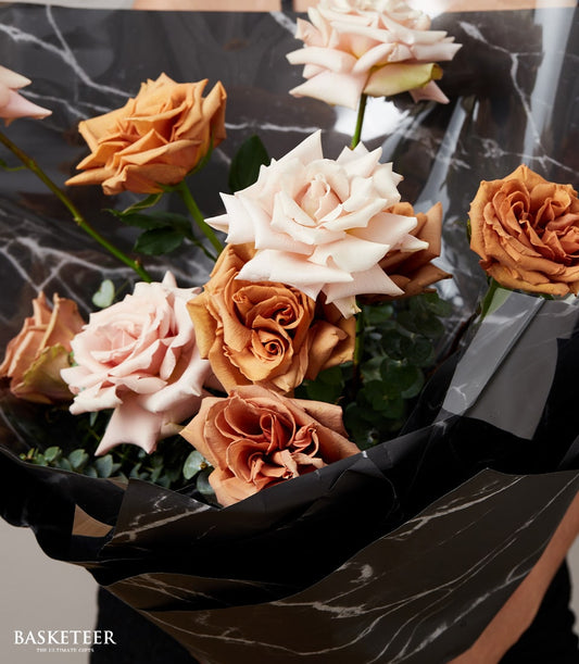 Warm-toned rose bouquet with peach and burnt orange blooms in black patterned wrapping, Valentine's Day gift for him