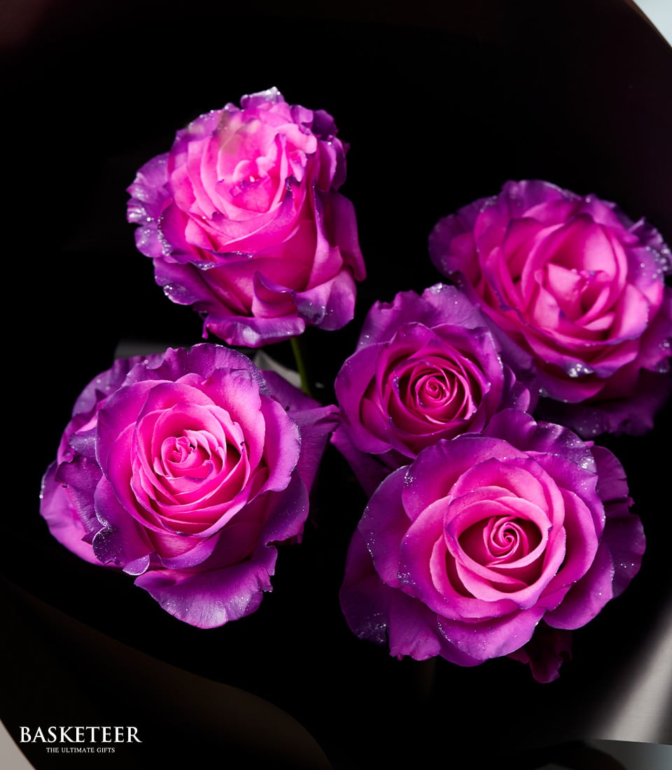 Vibrant purple and pink rose bouquet with fresh water droplets, wrapped in black for graduation gifting