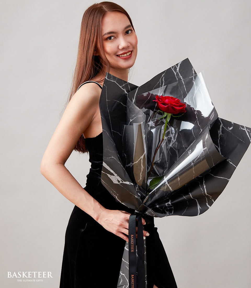 Single red rose in marble-patterned wrap with black ribbon, perfect for Valentine's Day gifting