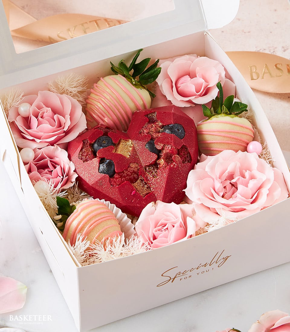 Red heart chocolate with rose petals, white chocolate strawberries, and fresh pink roses in luxury Valentine's gift box