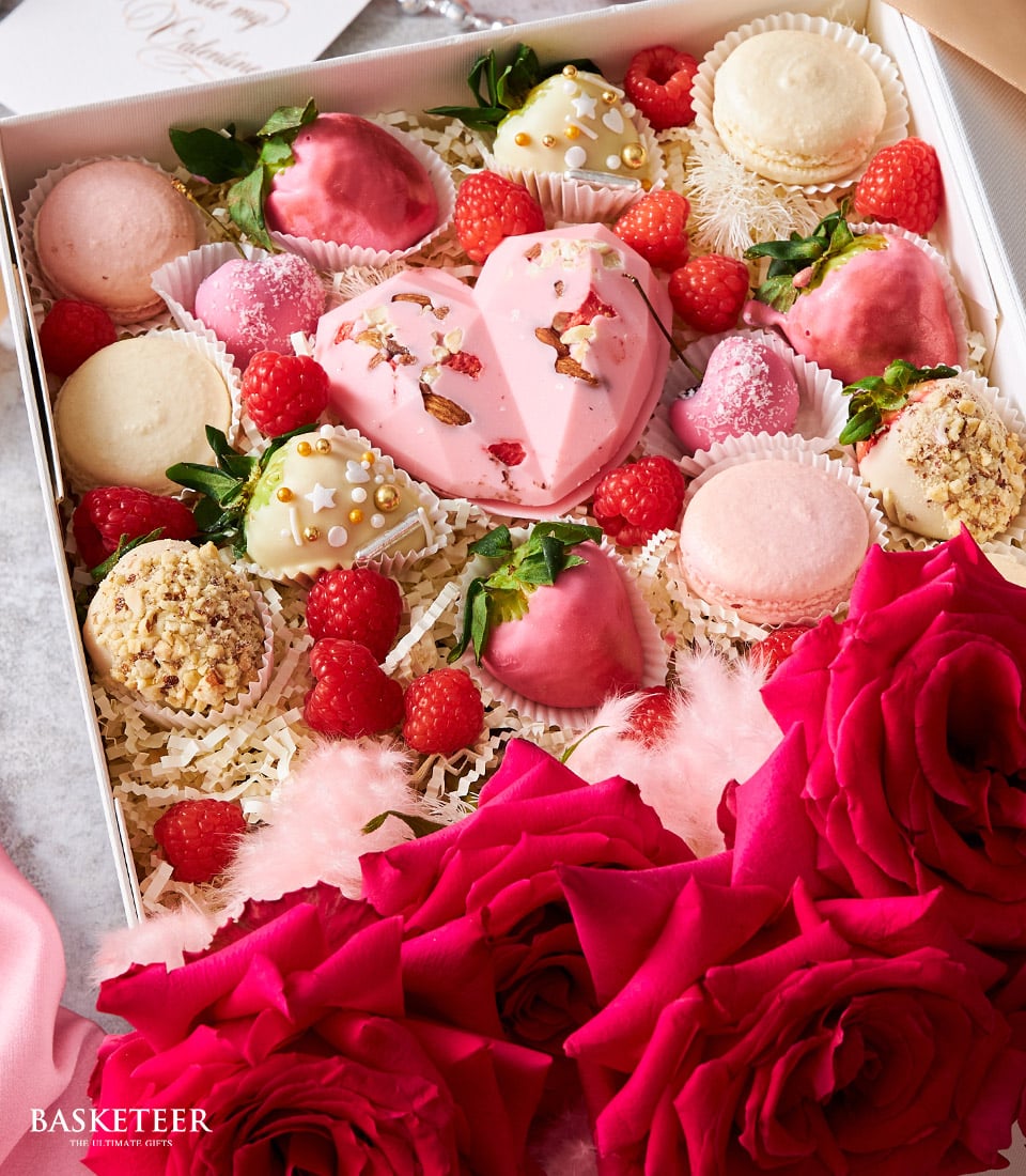 Deluxe pink heart dessert box with chocolate-covered strawberries, macarons, and fresh red roses for anniversaries