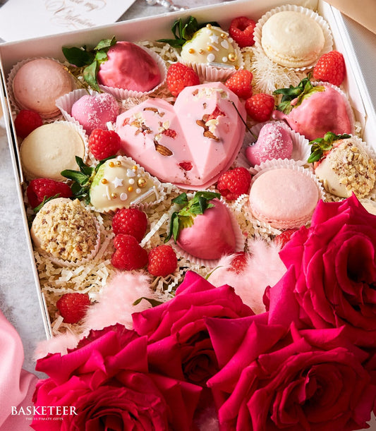 Deluxe pink heart dessert box with chocolate-covered strawberries, macarons, and fresh red roses for anniversaries