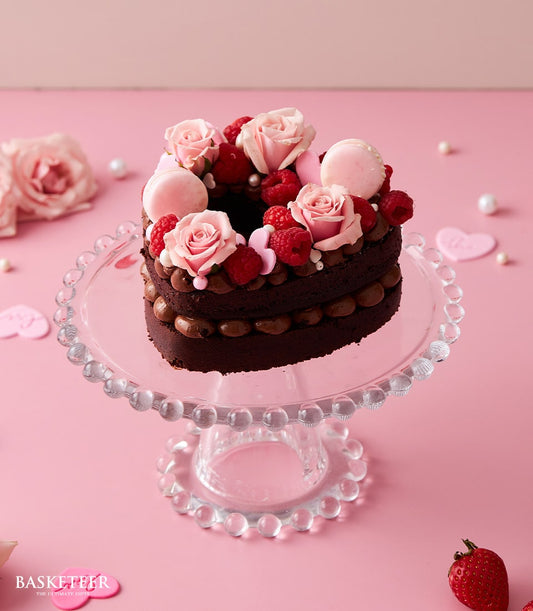 Heart-shaped dark chocolate cake with fresh roses, raspberries, and macarons on glass stand