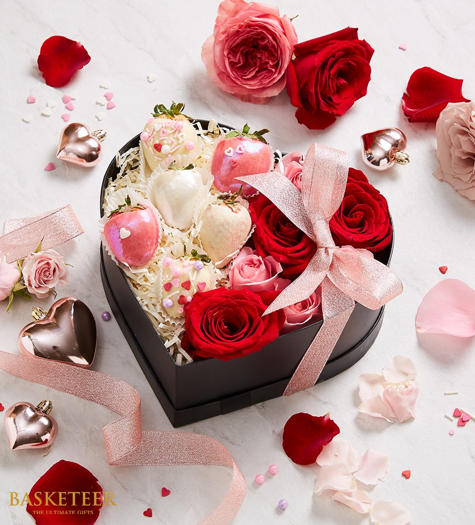 Black heart-shaped gift box with chocolate-covered strawberries, red roses, and rose gold ribbon for anniversary
