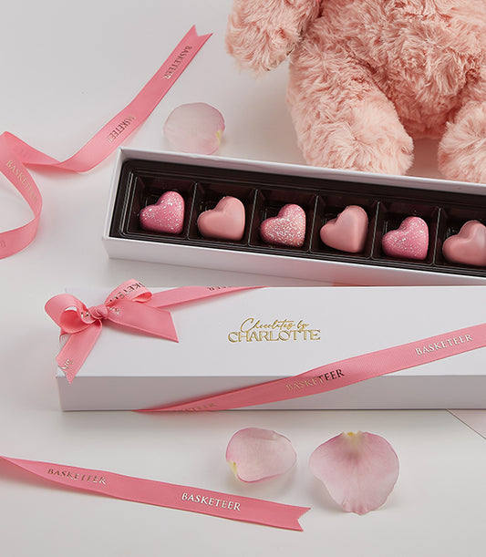 Luxury Valentine gift set with heart-shaped chocolates, pink teddy bear, and rose petals in ribbon-tied Basketeer box