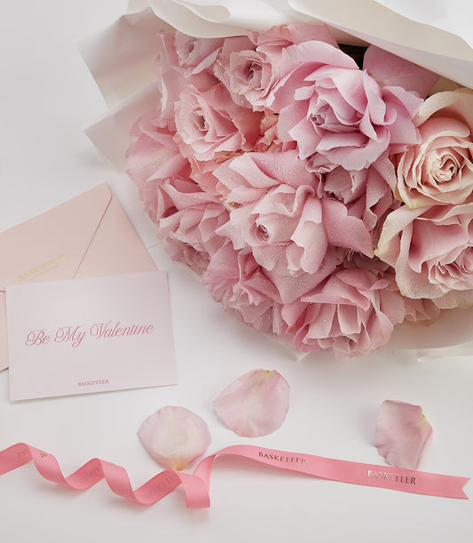 Fresh pink rose bouquet with white wrapping, matching Valentine card, and scattered petals